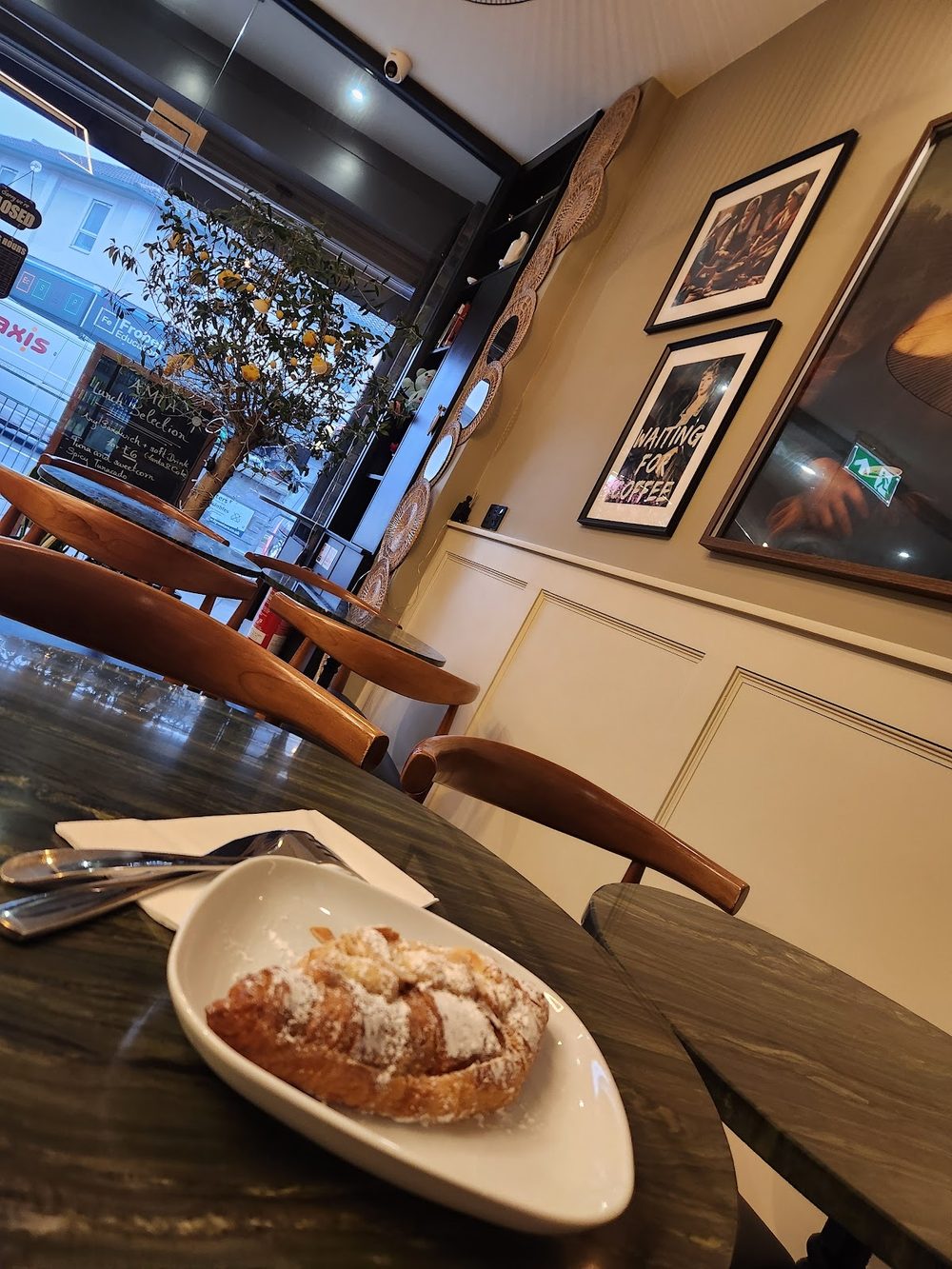 Inside the café, a window table set with coffee, wooden chairs and framed pictures on the wall.