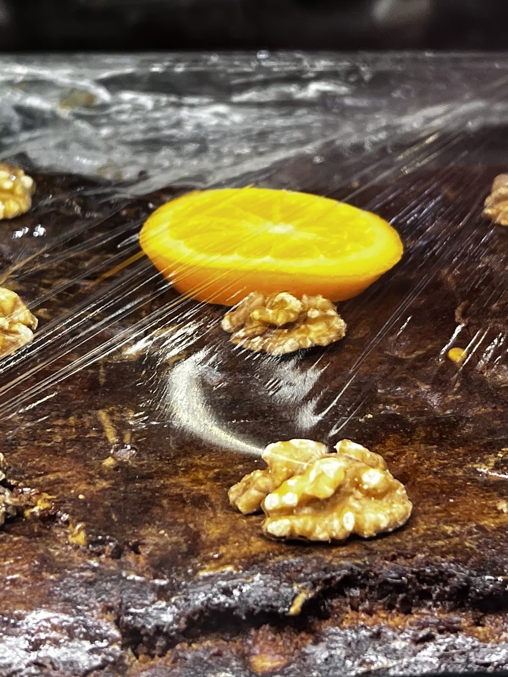 A close-up of dark walnut cake topped with walnut halves and a slice of orange.