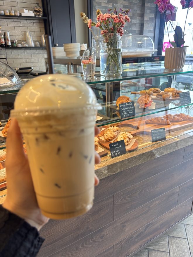 An iced coffee held up in front of the pastry display.
