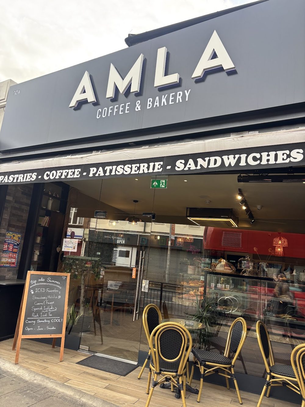 The AMLA Coffee & Bakery shopfront on Longbridge Road, with pavement tables outside the door.