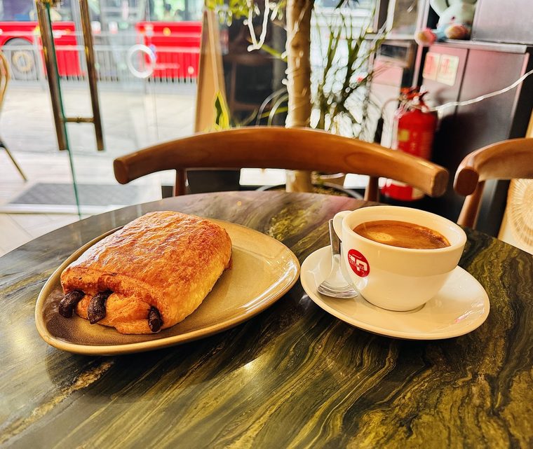 A pain au chocolat served on a plate with a coffee.
